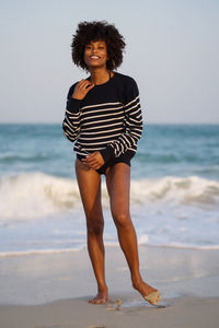 Young black woman standing by the sea wearing striped jumper