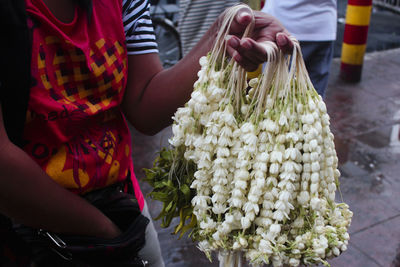 Cropped image of woman selling jasmine garlands on street in city