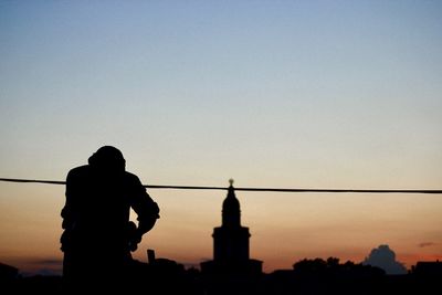 Silhouette man standing by building against sky during sunset