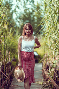 Young woman holding hat standing amidst plants