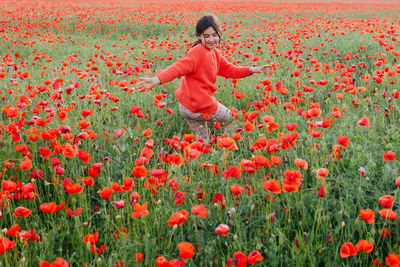 Girl in red clothes dancing in the middle of the poppy field