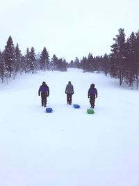 Rear view of people with sleds on snowy field