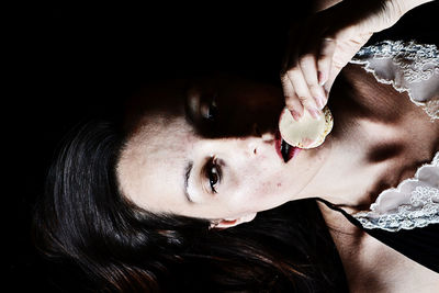 Close-up of woman eating food against black background