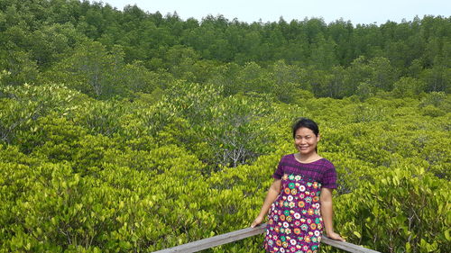 Portrait of young woman standing against green plants