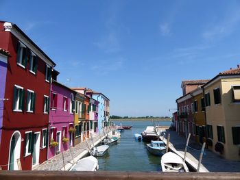 Boats moored in sea by houses against sky