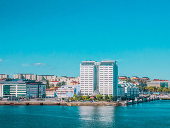 Sea by buildings against blue sky