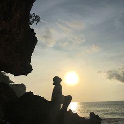 Silhouette person on rock by sea against sky during sunset