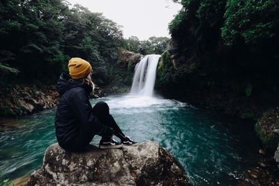 Woman sitting on rock by waterfall