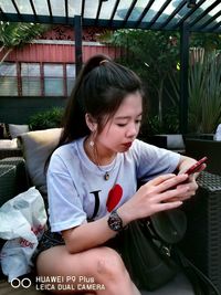 Young woman using mobile phone while sitting on laptop