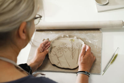 Woman rolling clay, making ceramic plate in studio with floral pattern. handmade creative work