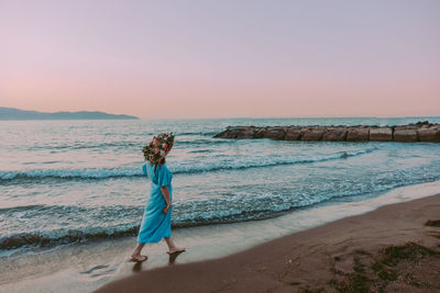 Woman standing on beach against sky during sunset