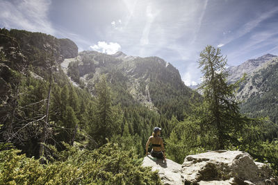 Rear view of woman sitting on cliff against mountain range