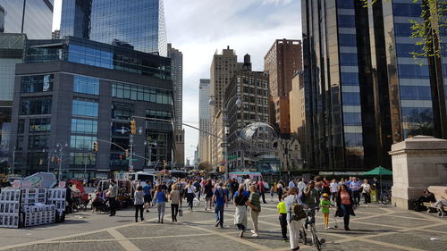 People on city street by buildings against sky