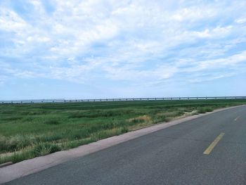 Empty road amidst field against sky