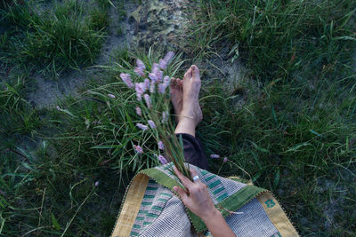 Low section of woman holding flowers on grassy field