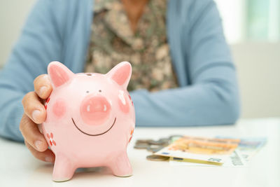 Midsection of man with piggy bank on table