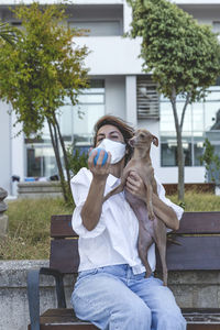 Portrait of woman sitting with dog on bench outdoors