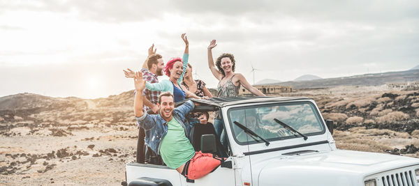 Happy friends in car against sky