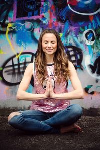 Woman smiling while meditating against graffiti wall