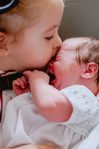 Closeup of crop caring little girl hugging and kissing crying newborn baby sibling