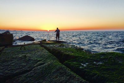 Silhouette man fishing on beach against clear sky during sunset