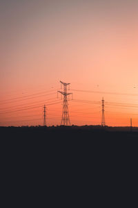Silhouette electricity pylons on field against sky during sunset
