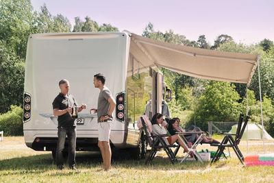 Senior man talking to son while family relaxing outside van at campsite