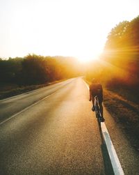 Rear view of man riding bicycle on road against sky during sunset