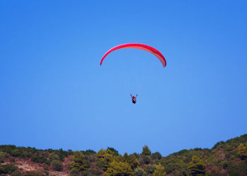 Low angle view of paragliding against clear blue sky