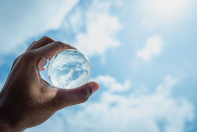 Cropped image of hand holding crystal ball against sky