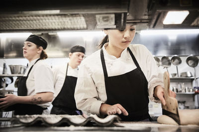 Female chef student cutting dough in commercial kitchen