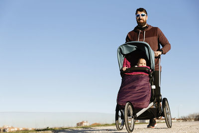 Man walking with baby stroller on road against sky