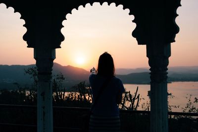 Rear view silhouette woman pointing at sun while standing in balcony