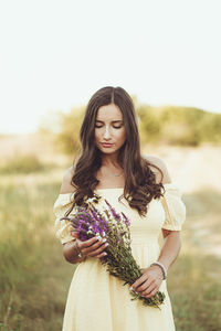Beautiful young woman holding flower bouquet
standing against plants