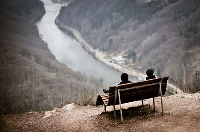 Rear view of people sitting on bench by saar river