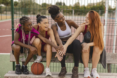 Cheerful young women stacking hands sitting at sports court