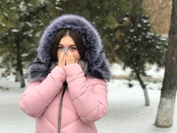 Portrait of young woman wearing warm clothing while standing against trees during winter