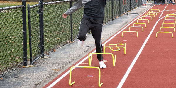 High school boy tripping over yellow mini hurdles while running a sports drill  at  track practice.