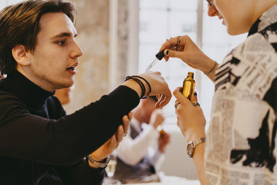 Non-binary person testing essential oil sample on male colleague's hand during event at convention center