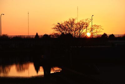 Silhouette trees by lake against orange sky