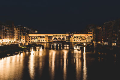 Illuminated bridge over river by buildings against sky at night