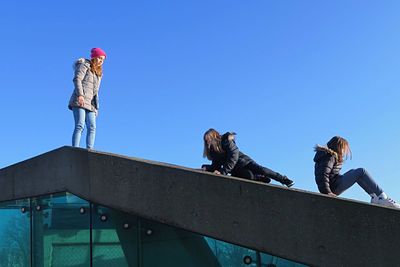 Friends enjoying on top of roof against clear blue sky