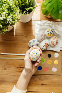 Female hand holding modern easter eggs painted. brushes and paints with flowers and plants.
