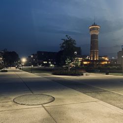 Illuminated street light by building against sky at dusk