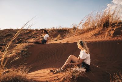 Friends sitting on desert against sky