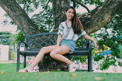 Portrait of young woman sitting on bench against tree