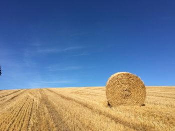 Hay bales on field against blue sky