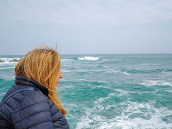 Side view of woman in warm clothing looking at beach against sky