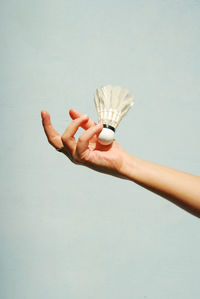 Close-up of woman hand holding shuttle cock against white background