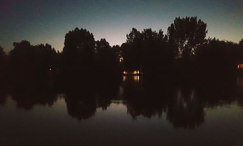 Silhouette trees by lake against sky during sunset